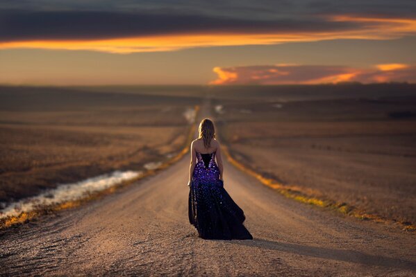 Ragazza cammina sulla strada per il tramonto in abito da sera