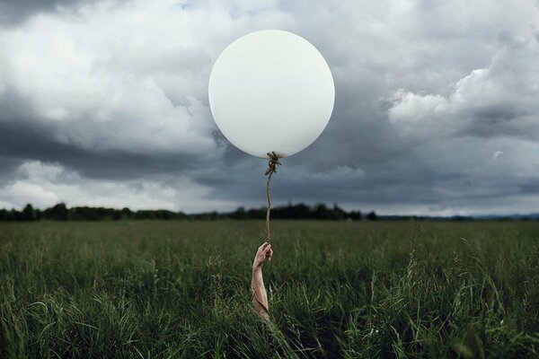 A hand in the field holds a ball. Cloudy weather