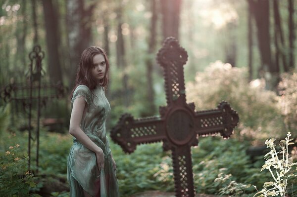 Mädchen schaut auf das Kreuz auf dem Friedhof