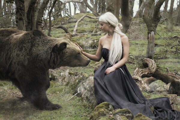 Chica en vestido negro en el bosque acaricia un oso