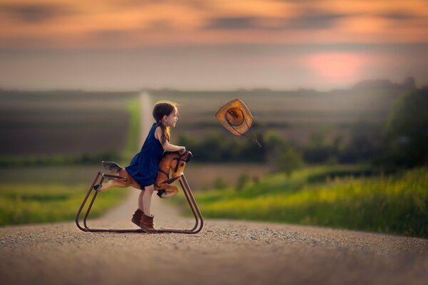 La fille est assise sur un jouet cheval, le chapeau удуло le vent