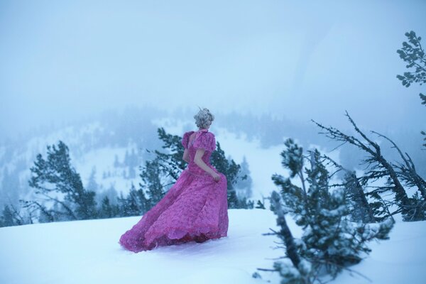 A girl in a pink long dress walking in the snow