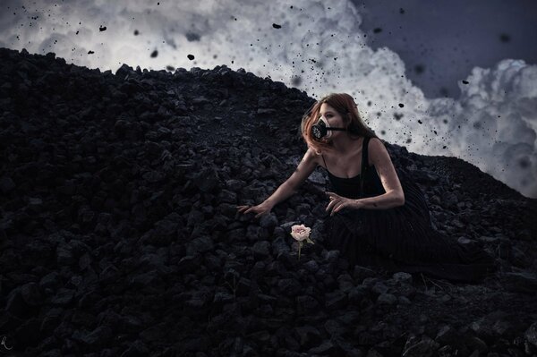 A girl in a black dress and a gas mask is sitting next to a flower