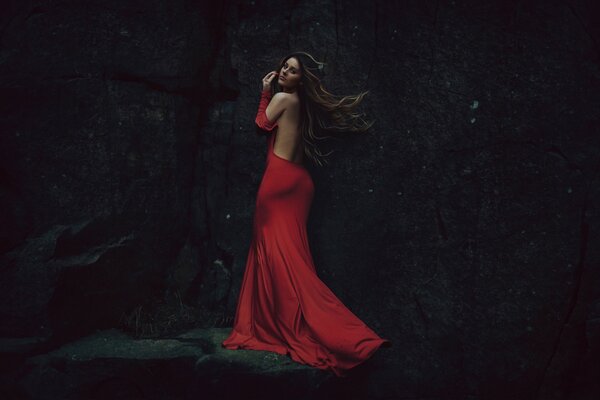 Schönes Mädchen im roten Kleid mit offenem Rücken auf dem Hintergrund eines dunklen Felsens