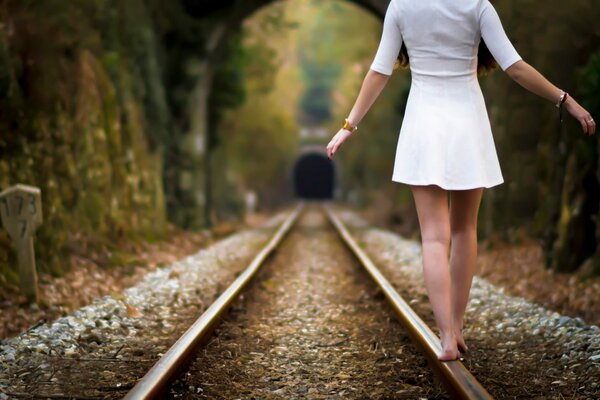 A girl in a dress walks on rails