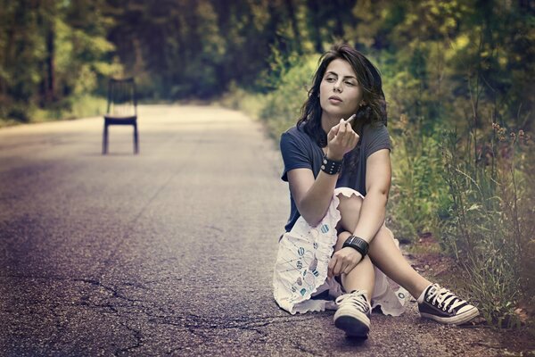 Une jeune femme est assise sur le bord de la route, sur la terre, et la fumée, au milieu de la route en vaut la chaise