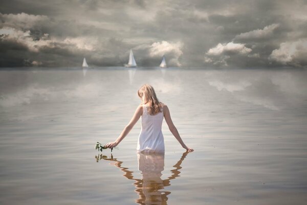 The girl is standing in the water. Sails at sea