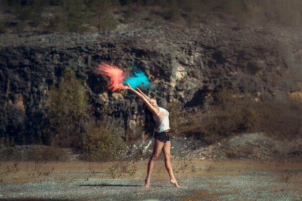 A slender girl is standing on the ground. Colorful dust is flying out of her hands