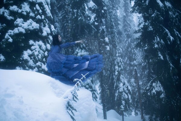 A girl in a blue dress on the background of fir trees in the snow