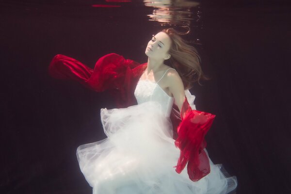 A girl in a white dress with a red scarf under water