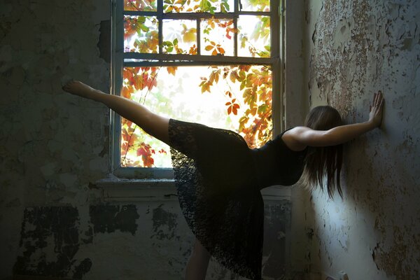 Mädchen in Ballettpose in einem schwarzen Kleid an der Wand