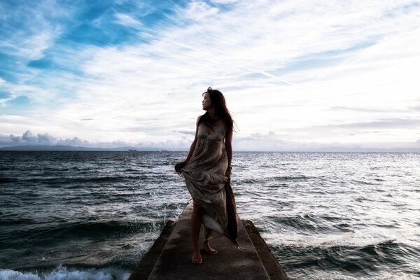 A girl in a dress stands on the pier