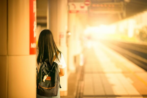 Una ragazza con uno zaino in piedi alla stazione ferroviaria e in attesa di un treno