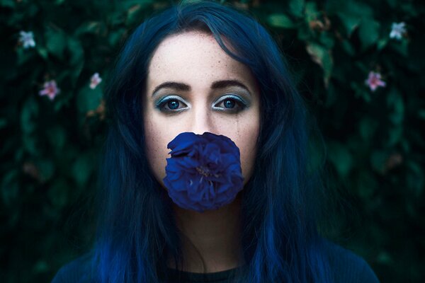 A girl in blue shades holds a blue flower with her lips