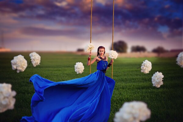 The blue dress flutters from the swing of the girl on the swing