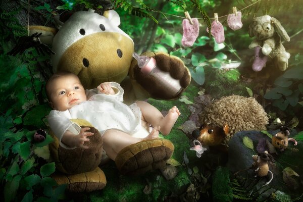 The baby is sitting on a toy among the greenery