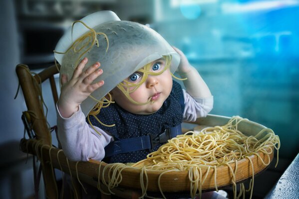 Kleines Kind mit einem Teller Spaghetti auf dem Kopf