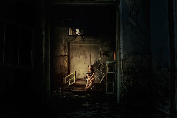 A girl is sitting on the threshold of an abandoned house