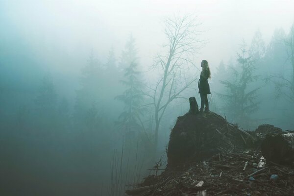 A girl with a dog on a hill in a foggy forest