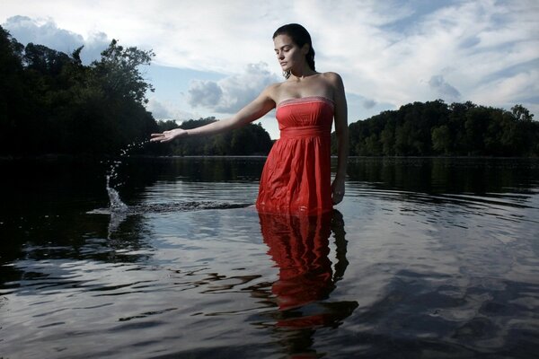 Ragazza bruna in abito rosso è in piedi fino al ginocchio in acqua