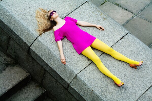 A bright girl in colorful clothes and glasses on the parapet