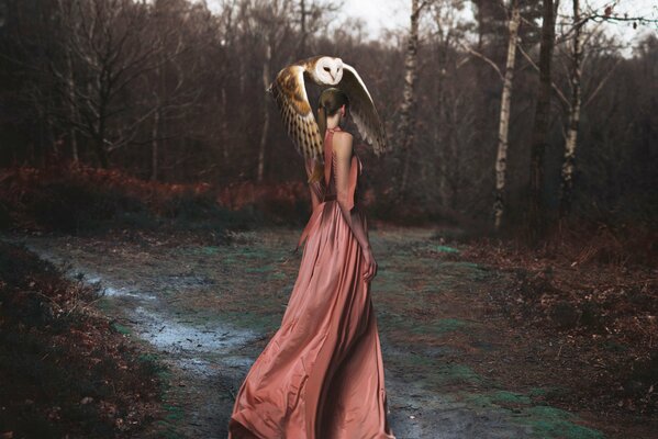 Mysterious photo of a girl in a pink dress in the forest with an owl