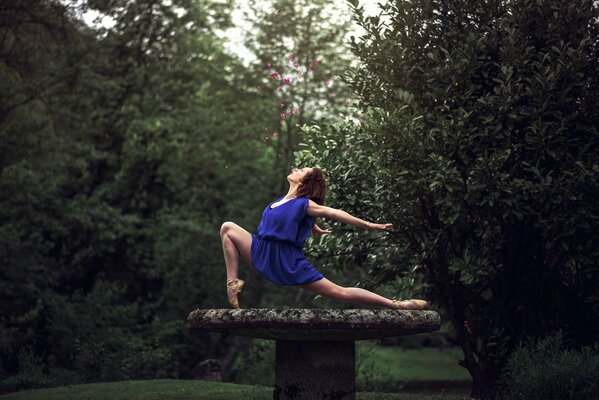 A girl in a blue dress does exercises in the forest