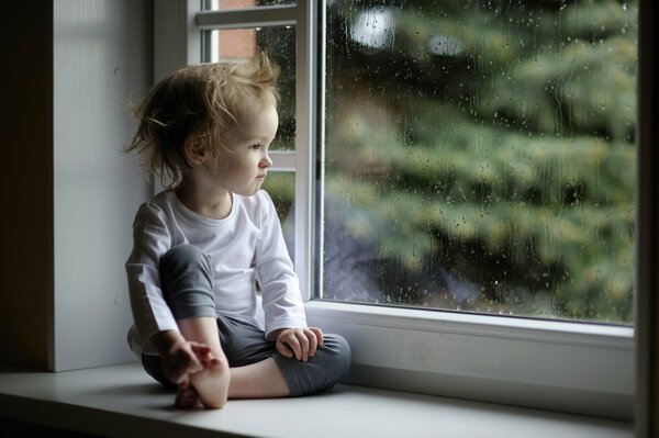 Niño mirando por la ventana en la lluvia