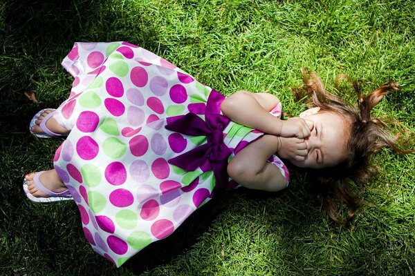 Una niña en la hierba yace riendo bajo el sol