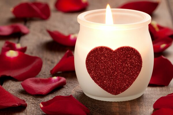 A candle with a red heart surrounded by rose petals