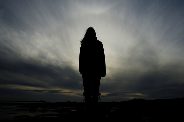 Dunkle menschliche Figur auf grauem Hintergrund mit Wolken