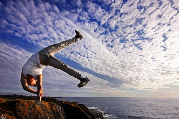 A man stands on one hand on the edge of a cliff