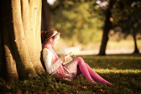 Una niña se sienta debajo de un árbol y Lee un libro