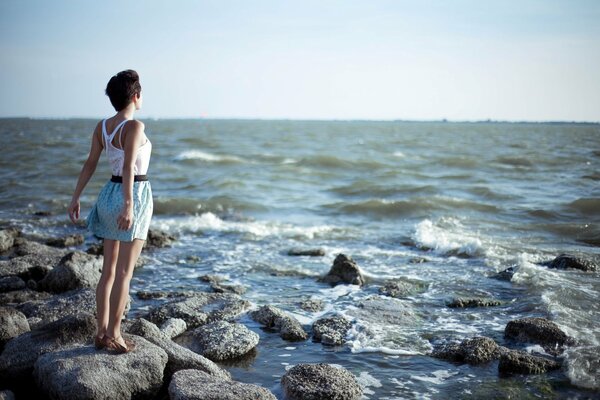 Sea breeze. A girl stands on a rocky shore