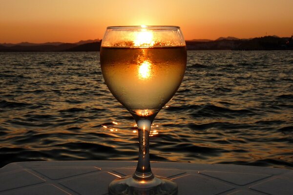 Glas mit Wasser auf dem Hintergrund des Meeres mit Sonnenuntergang