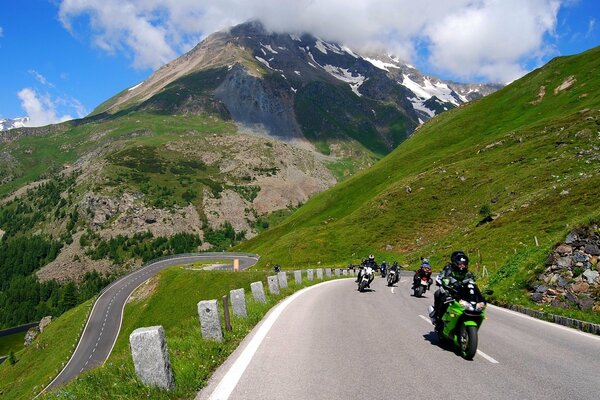 A group of bikers rides along the road among the mountains