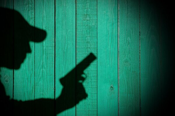 La sombra de un hombre con una pistola sobre un fondo de madera verde