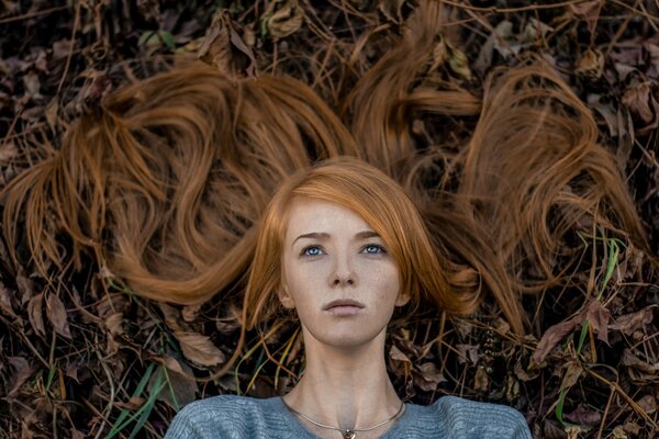 Portrait of a girl with red hair on a background of fallen leaves