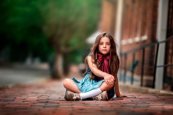 Petite fille dans une robe et un arc autour du cou est assis