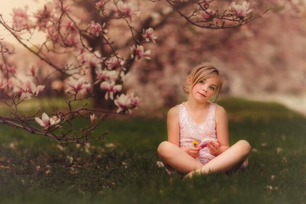 Niña con una manzana en primavera bajo las flores de un árbol