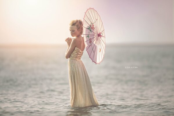 Jeune fille debout dans la mer avec un parapluie