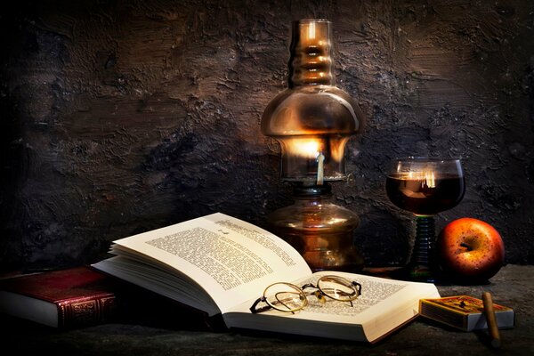 Dark still life with a book lamp a glass of wine and an apple