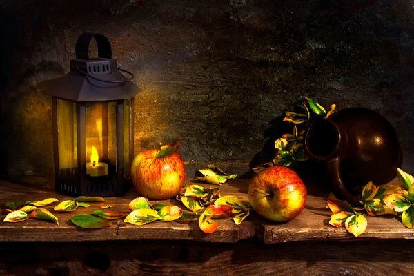 Apples are warmed by the glow of a lantern near the jug