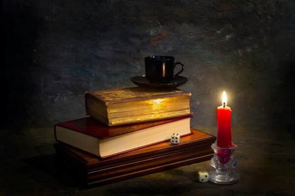 A candle illuminates books and a mug on the table