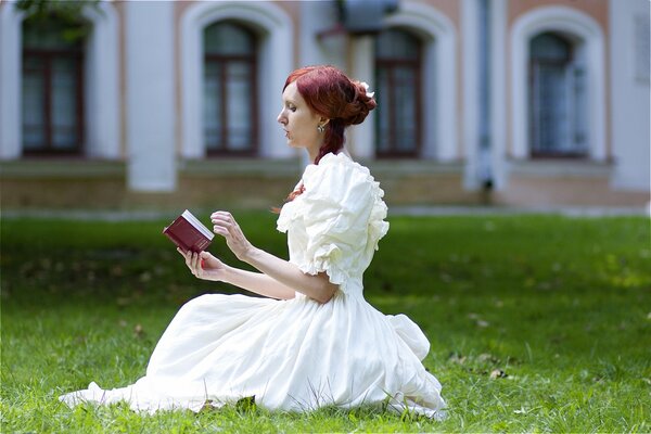 Chica con vestido blanco en el césped leyendo un libro