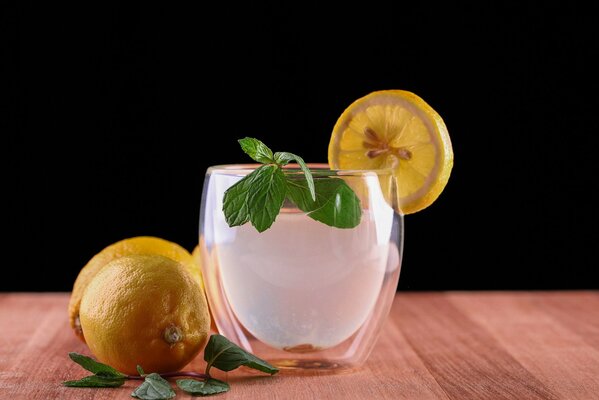 Sul tavolo c è un bicchiere con ghiaccio, una fetta di limone e menta, accanto ci sono limoni e rametti di menta