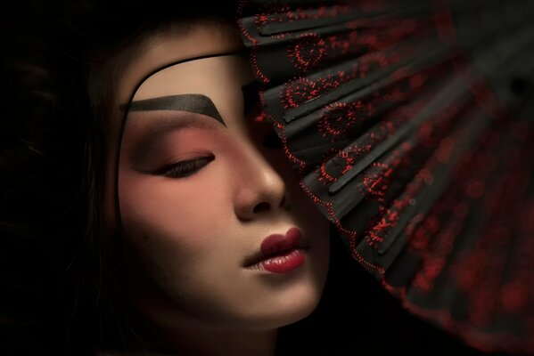 A geisha with beautiful makeup covers herself with a fan