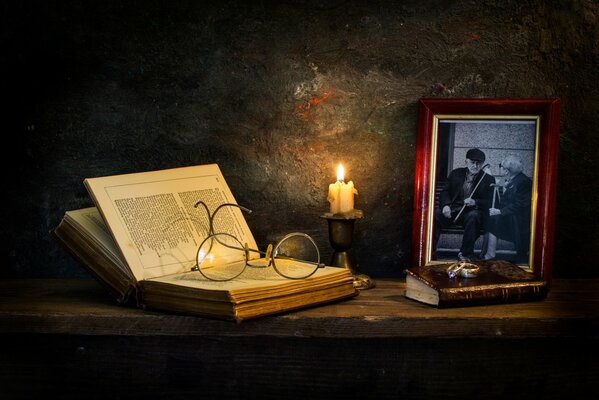 Libro con gafas en la mesa alrededor de una vela y fotos enmarcadas