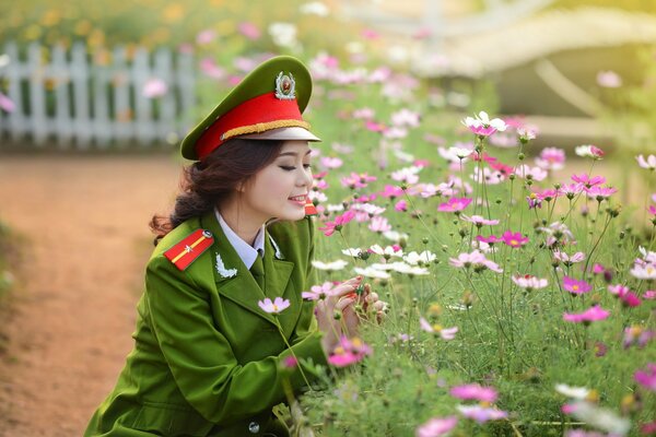 A girl in a military uniform is sitting near a field of flowers