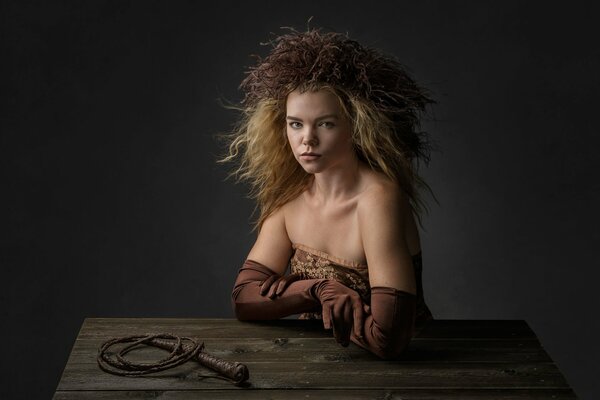 Portrait of a girl at a table with gloves and a whip